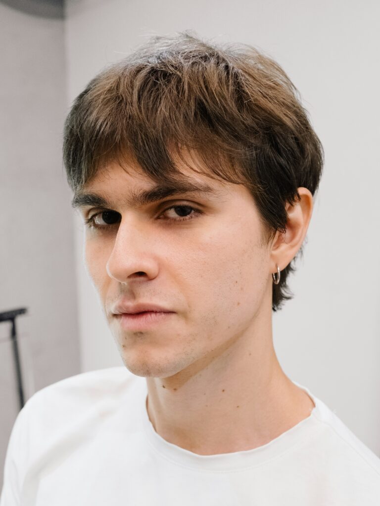 [ALT_TEXT: Un joven con un corte mullet de oficina, vestido con camiseta blanca.]