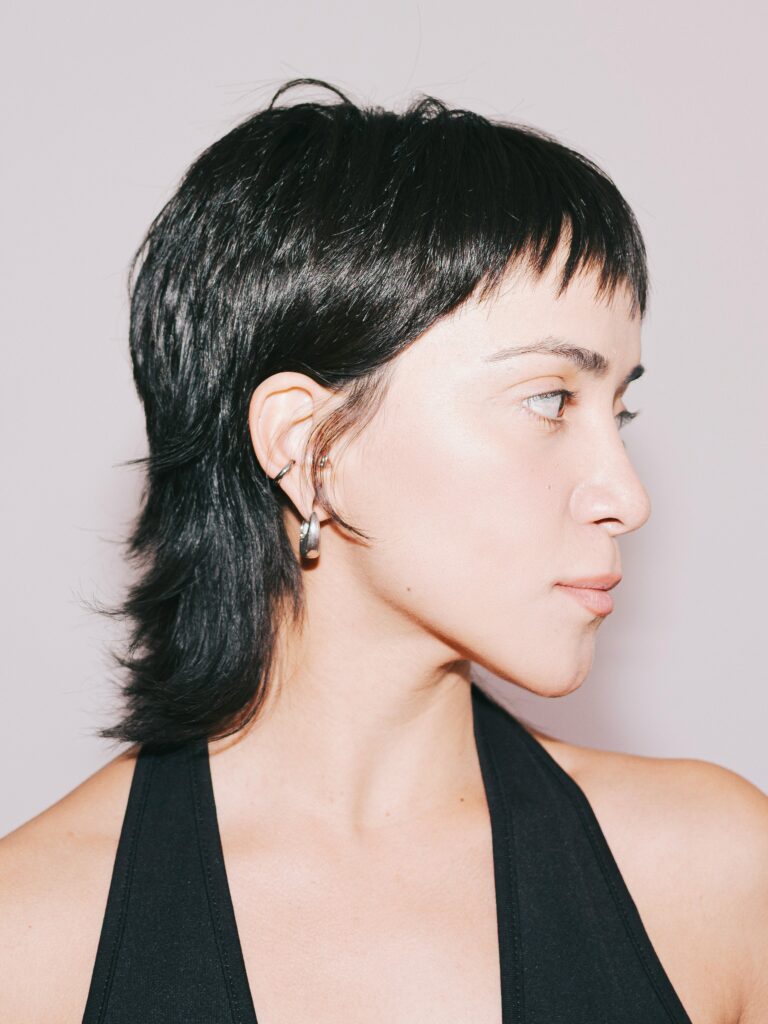 [ALT_TEXT: Una joven con un corte mullet elegante, vestida con un top negro de cuello halter.]