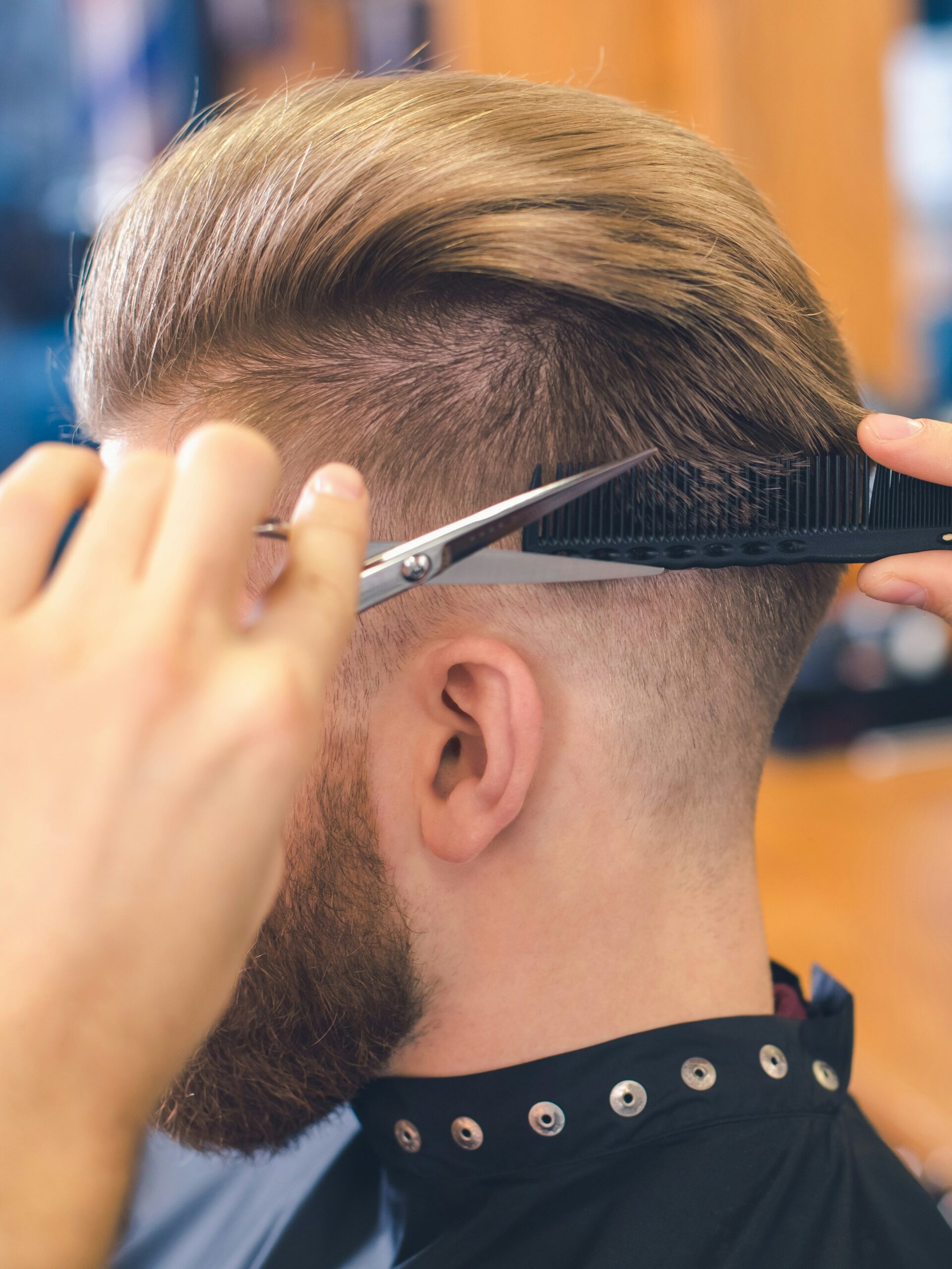Primer plano de un barbero haciendo un taper fade con la técnica de tijera sobre peine en la parte posterior de la cabeza