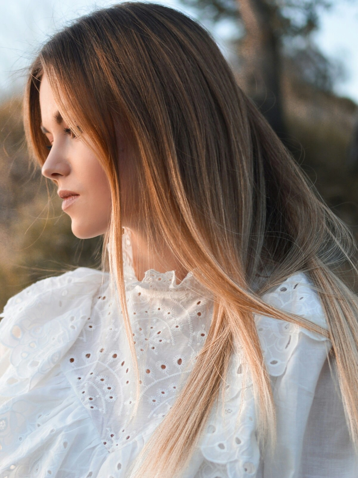 Vista lateral de una mujer al aire libre en un entorno natural, con balayage sobre pelo liso en el que el castaño se difumina en tonos rubios