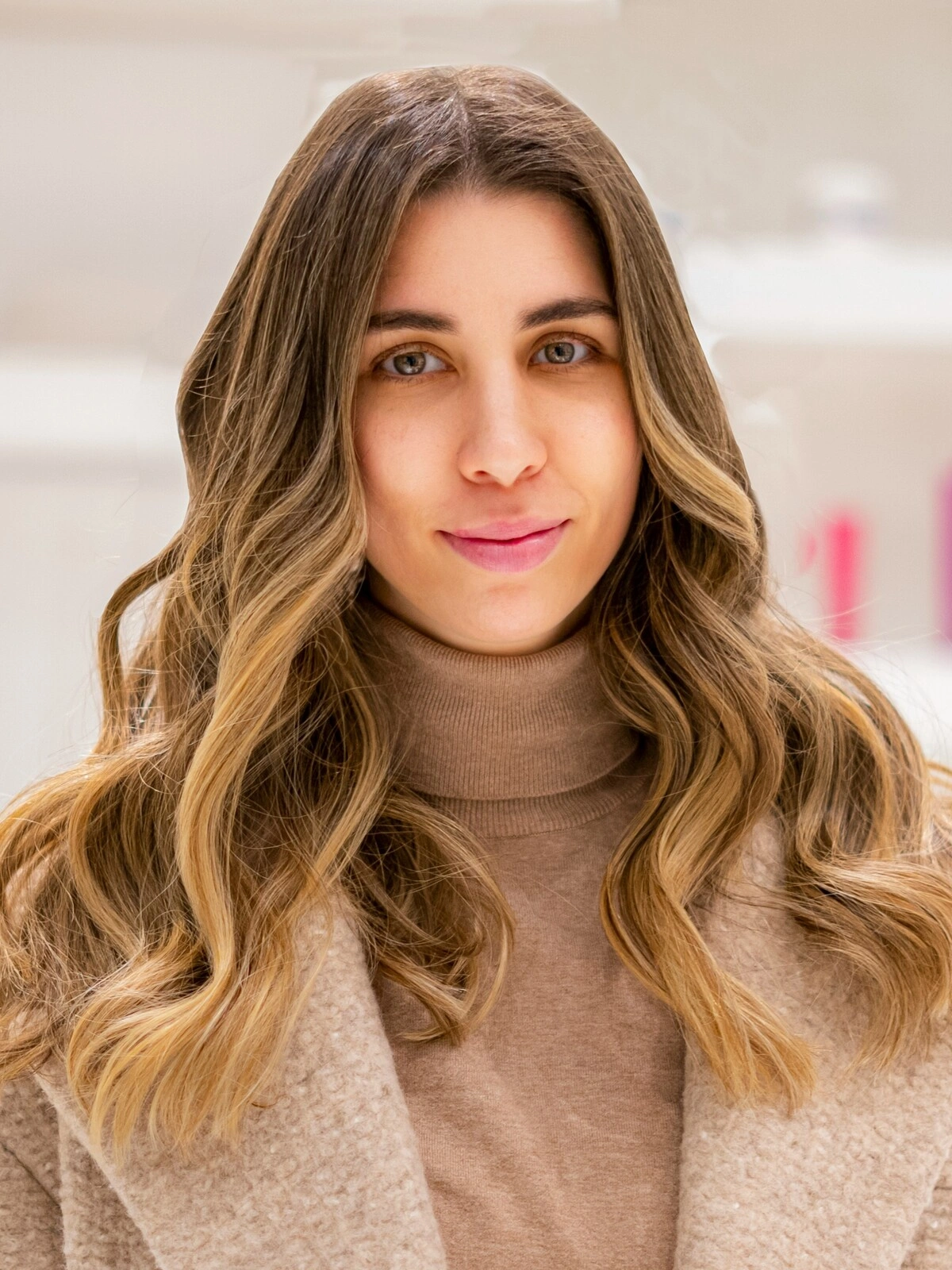 Una mujer con un jersey de cuello alto y un abrigo de lana color camel, con un balayage suave y ondulado en el que el castaño se difumina en tonos caramelo