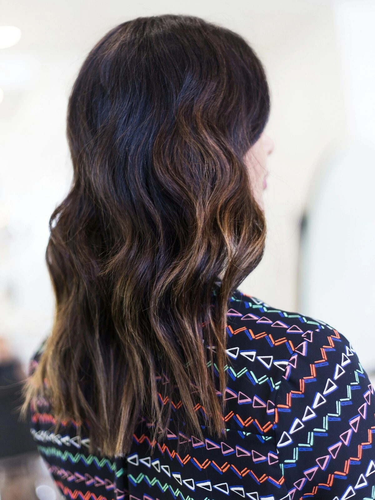 Vista trasera de la cabeza de una mujer con balayage en ondas suaves, en el que el pelo negro se difumina en tonos castaños cálidos