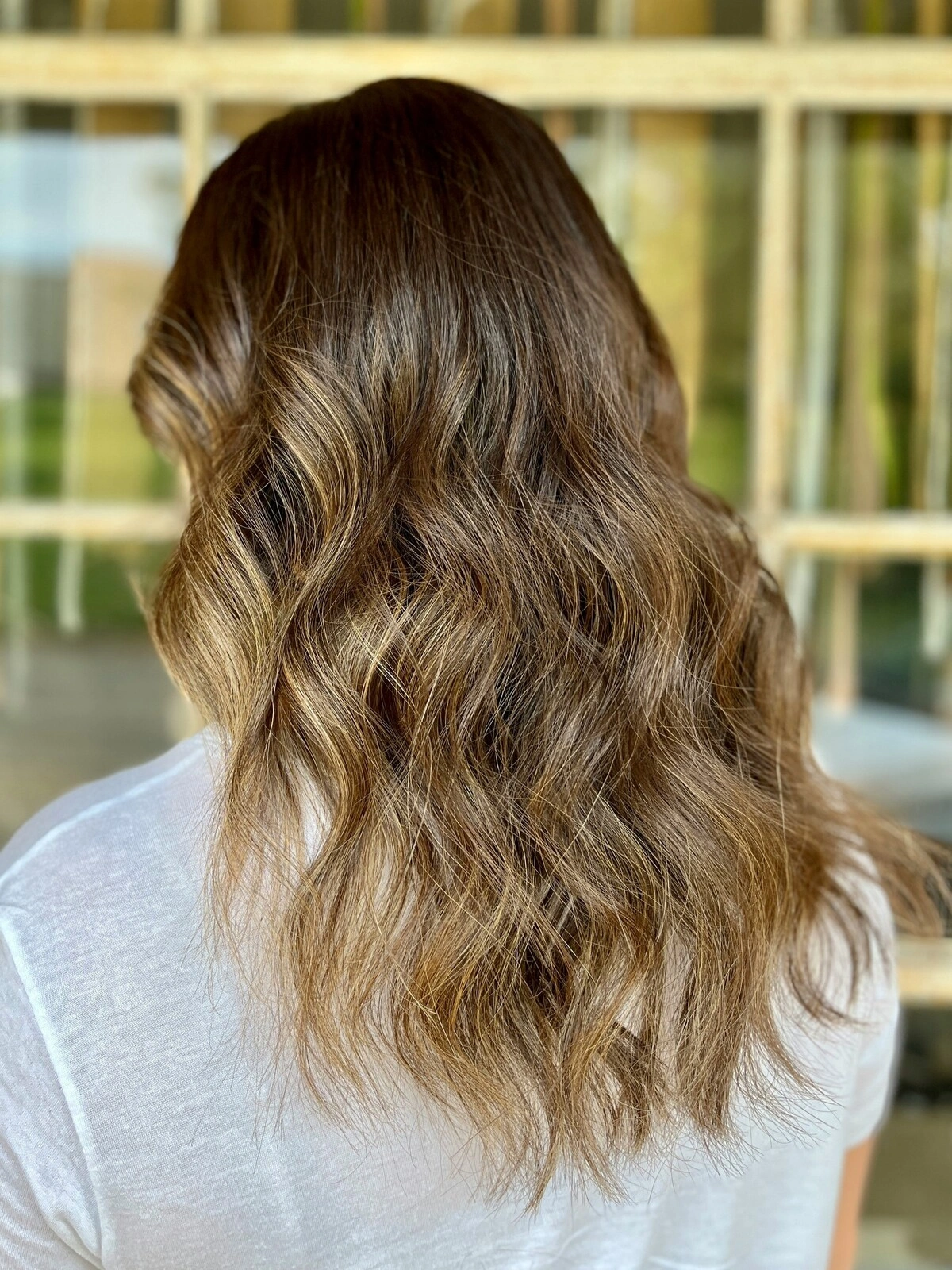 Vista trasera de la cabeza de una mujer con el pelo ondulado con balayage, en el que el color oscuro se difumina en tonos cálidos
