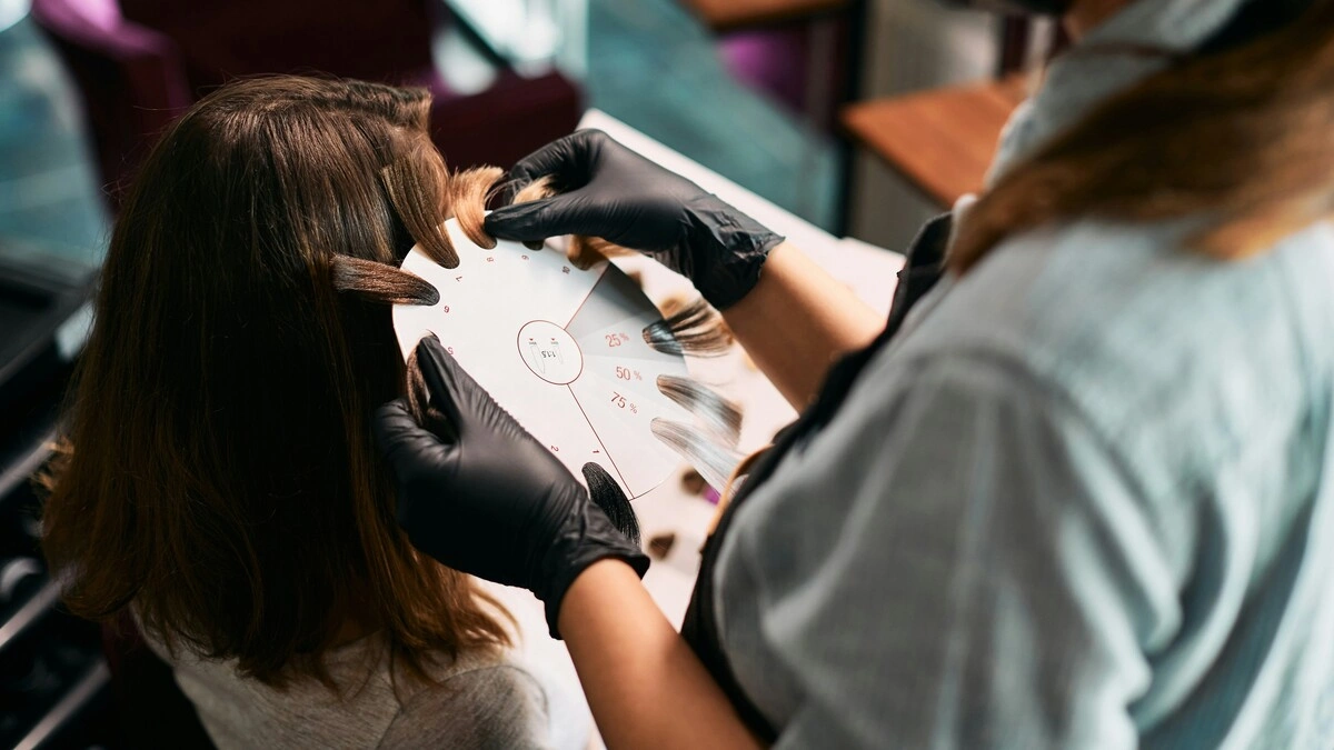 Primer plano de una colorista que acerca unas muestras de mechones a la cabeza de una clienta para elegir los tonos del balayage