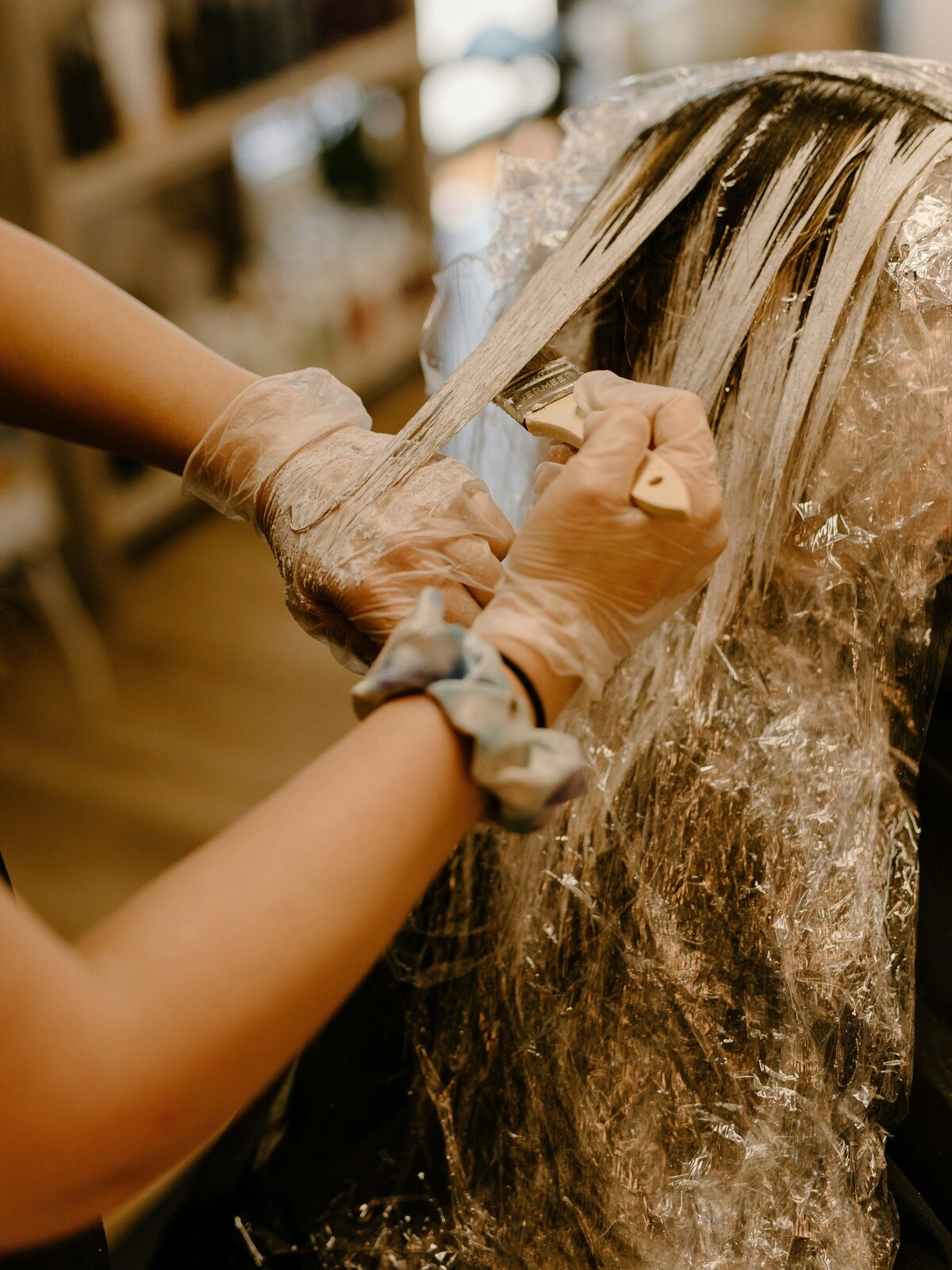 Una colorista con guantes aplica el color con un pincel sobre el pelo de una clienta, durante un balayage