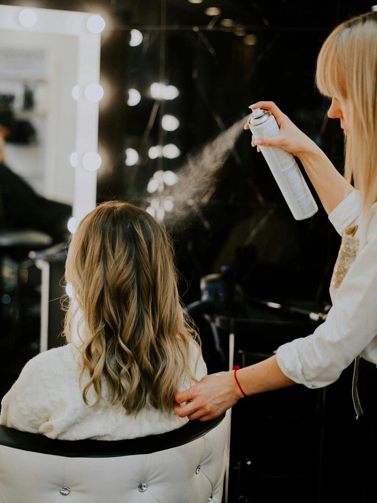 Una peluquera aplica un producto de acabado con espray sobre el pelo de una clienta tras un balayage, el secado y el peinado en ondas