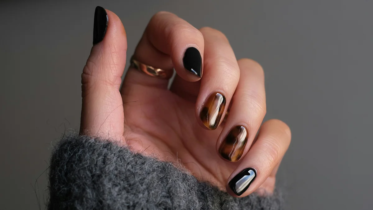 Primer plano de una mano con uñas cortas y una manicura de gel brillante en tonos negros y de estampado animal
