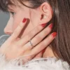 Primer plano de perfil de una mujer morena que se toca la cara y luce una manicura de gel roja y brillante
