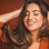 Primer plano de una mujer sonriendo con los ojos cerrados mientras pasa las manos por su pelo castaño, largo y suave