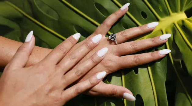 Foto de estudio de unas uñas acrílicas almendradas en tono nude recién hechas, sobre un fondo de hoja de palmera