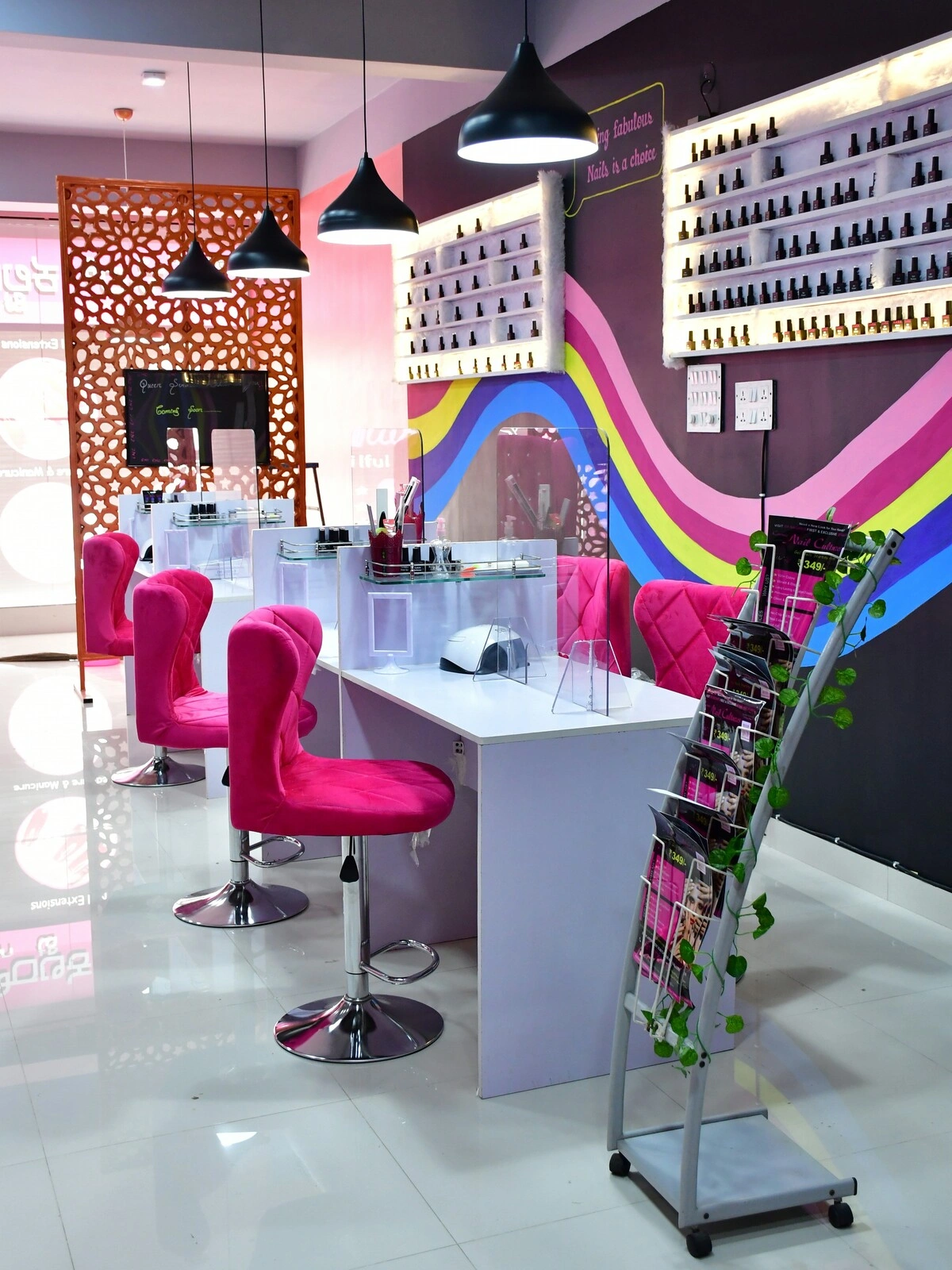Interior de un centro de uñas con mesas blancas limpias y ordenadas, sillas de terciopelo rosa y una pared morada