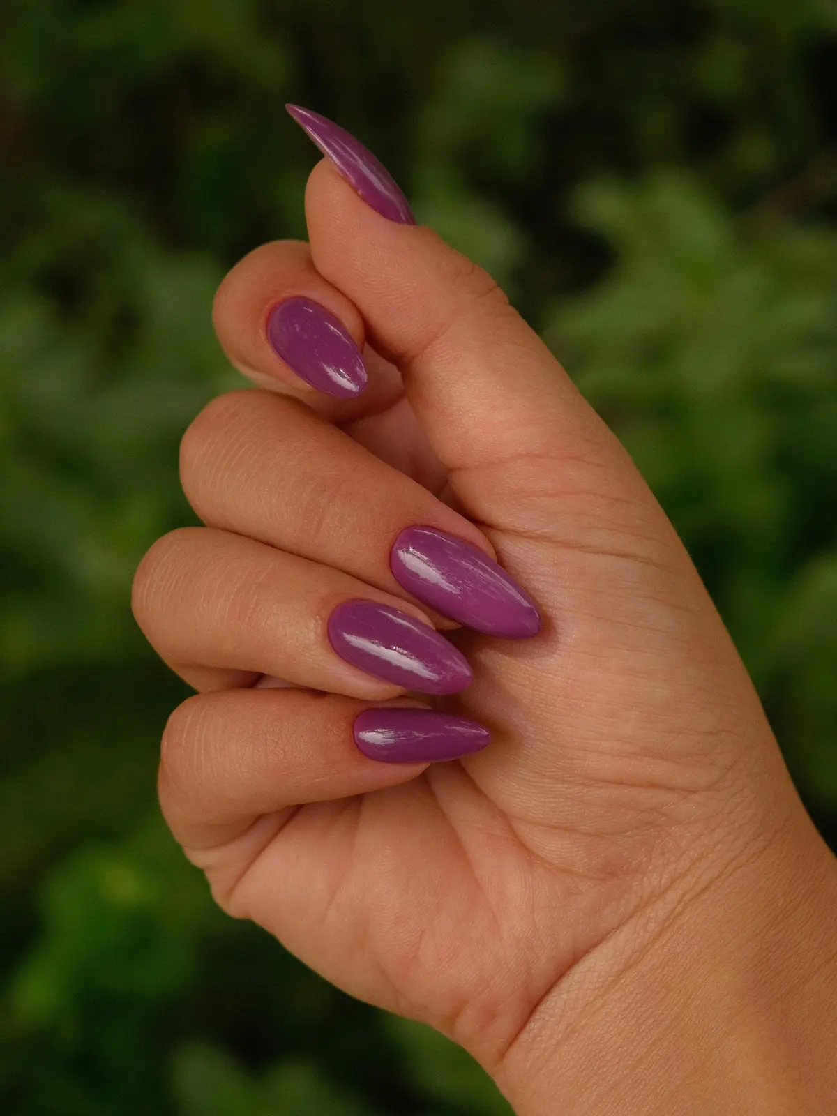 Primer plano de la mano de una mujer con uñas acrílicas almendradas de color morado
