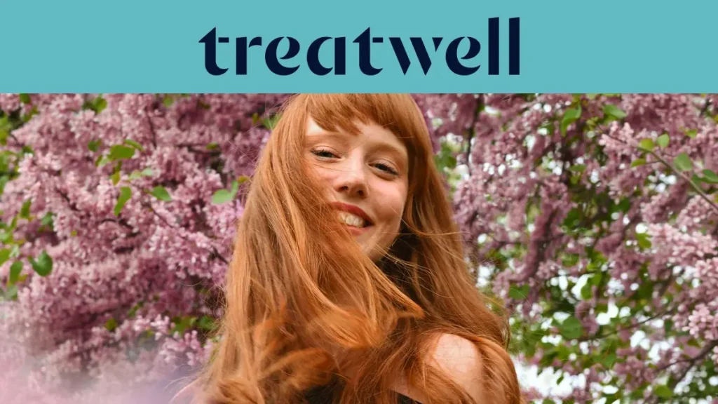 Primer plano de una mujer joven pelirroja y sonriente con flequillo, con el cabello moviéndose al viento frente a un fondo de flores de lila rosas. En la parte superior, una franja azul claro muestra el logotipo de "Treatwell" en azul oscuro.