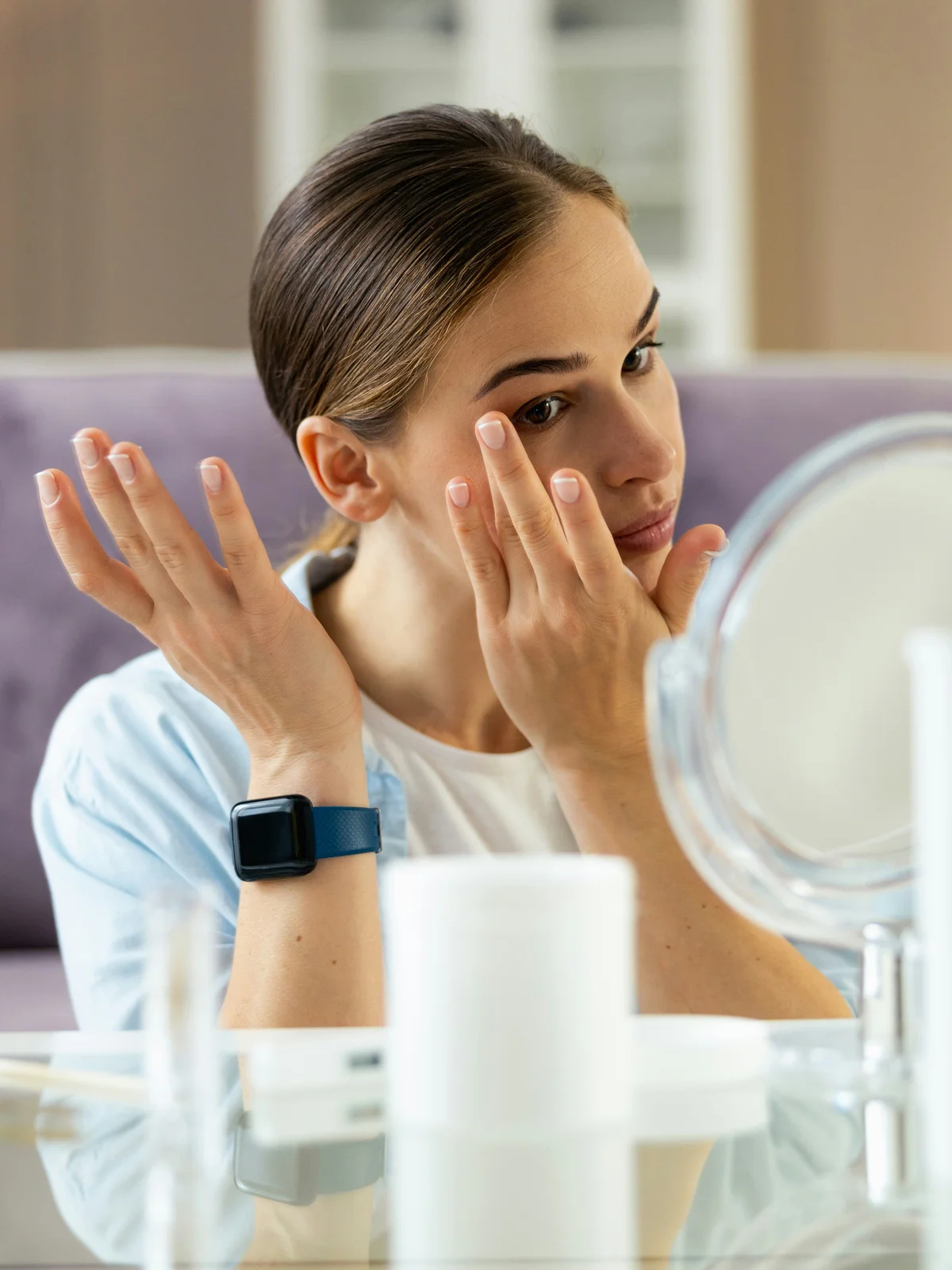 Una mujer sentada a una mesa se aplica con delicadeza crema hidratante y aceites en el rostro y las cejas