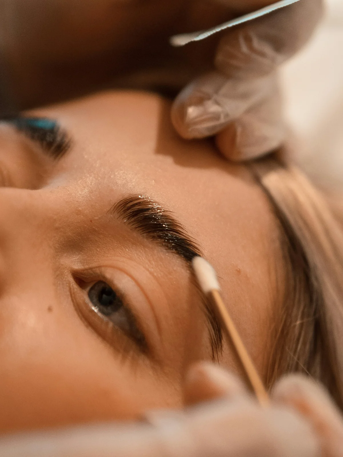 Primer plano de una clienta tumbada mientras una esteticista realiza un laminado de cejas
