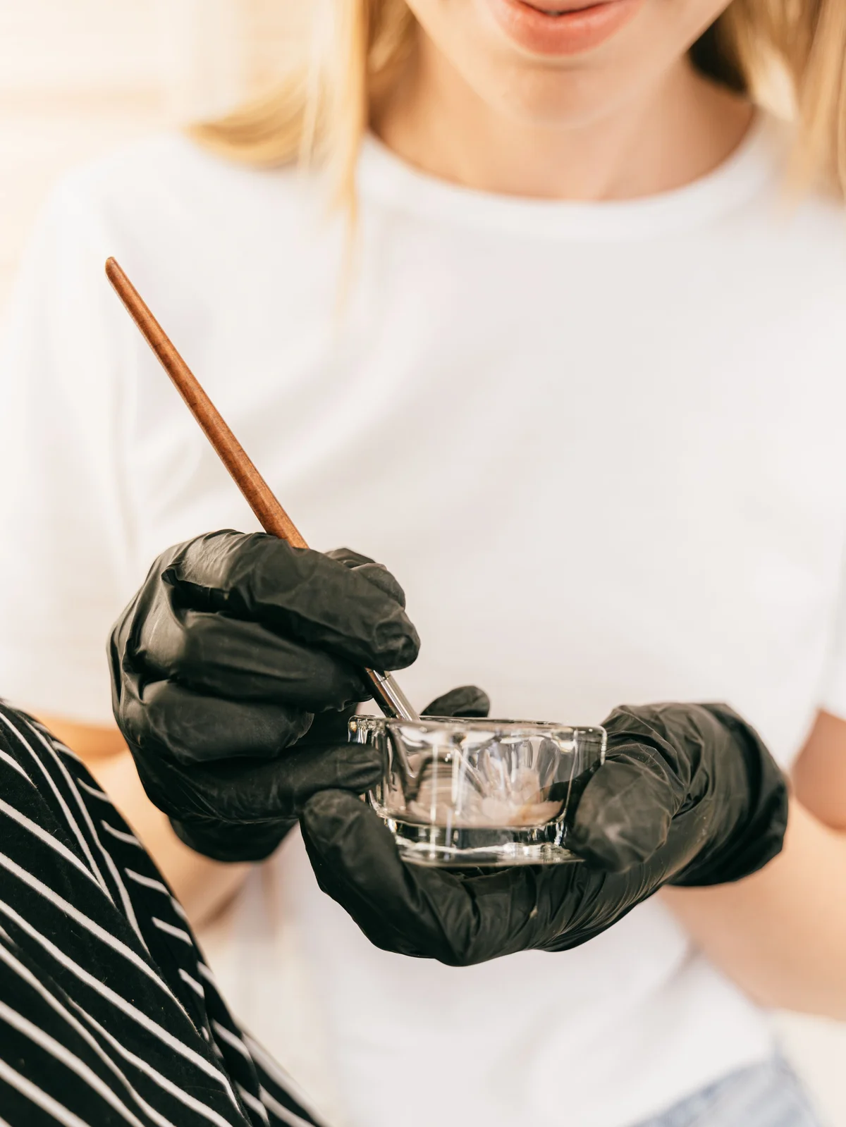 Primer plano de una esteticista sujetando un pequeño bote de cristal y un pincel fino mientras mezcla el tinte de cejas en el centro