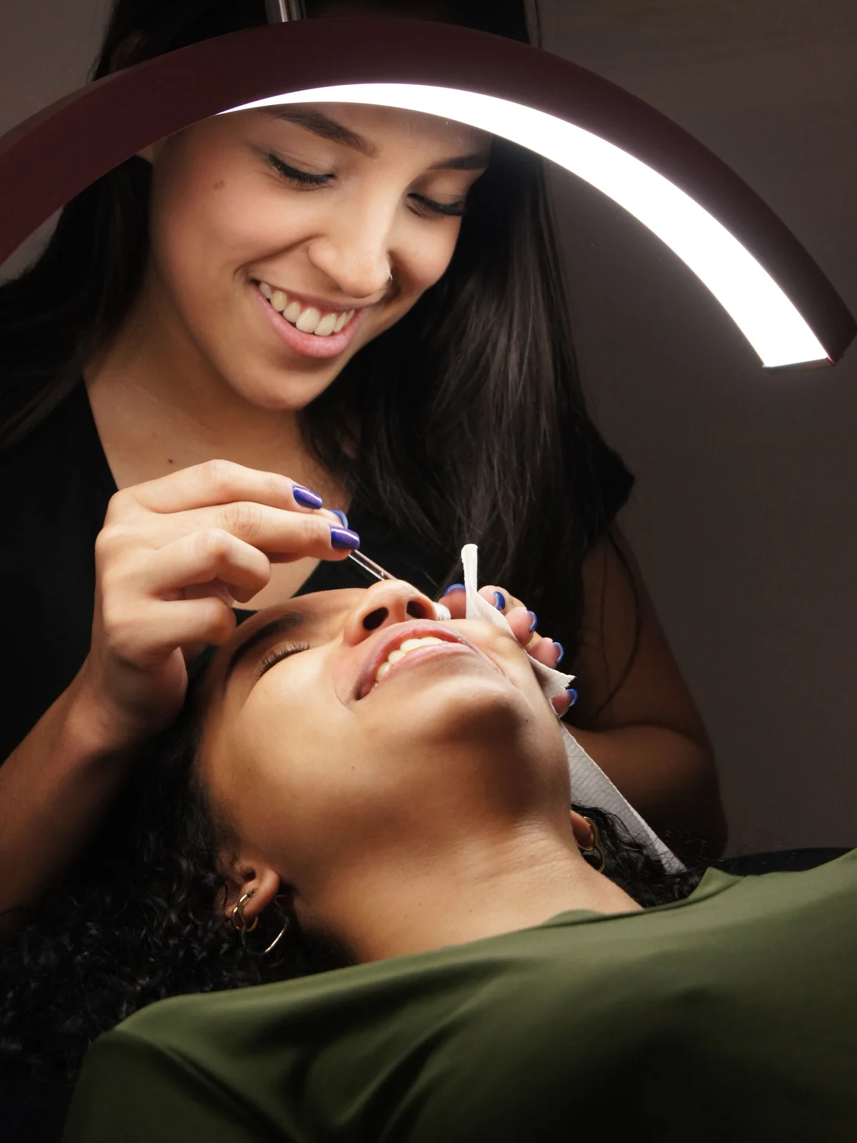 Primer plano de una esteticista aplicando tinte en las cejas de una clienta que descansa relajada en la camilla del centro
