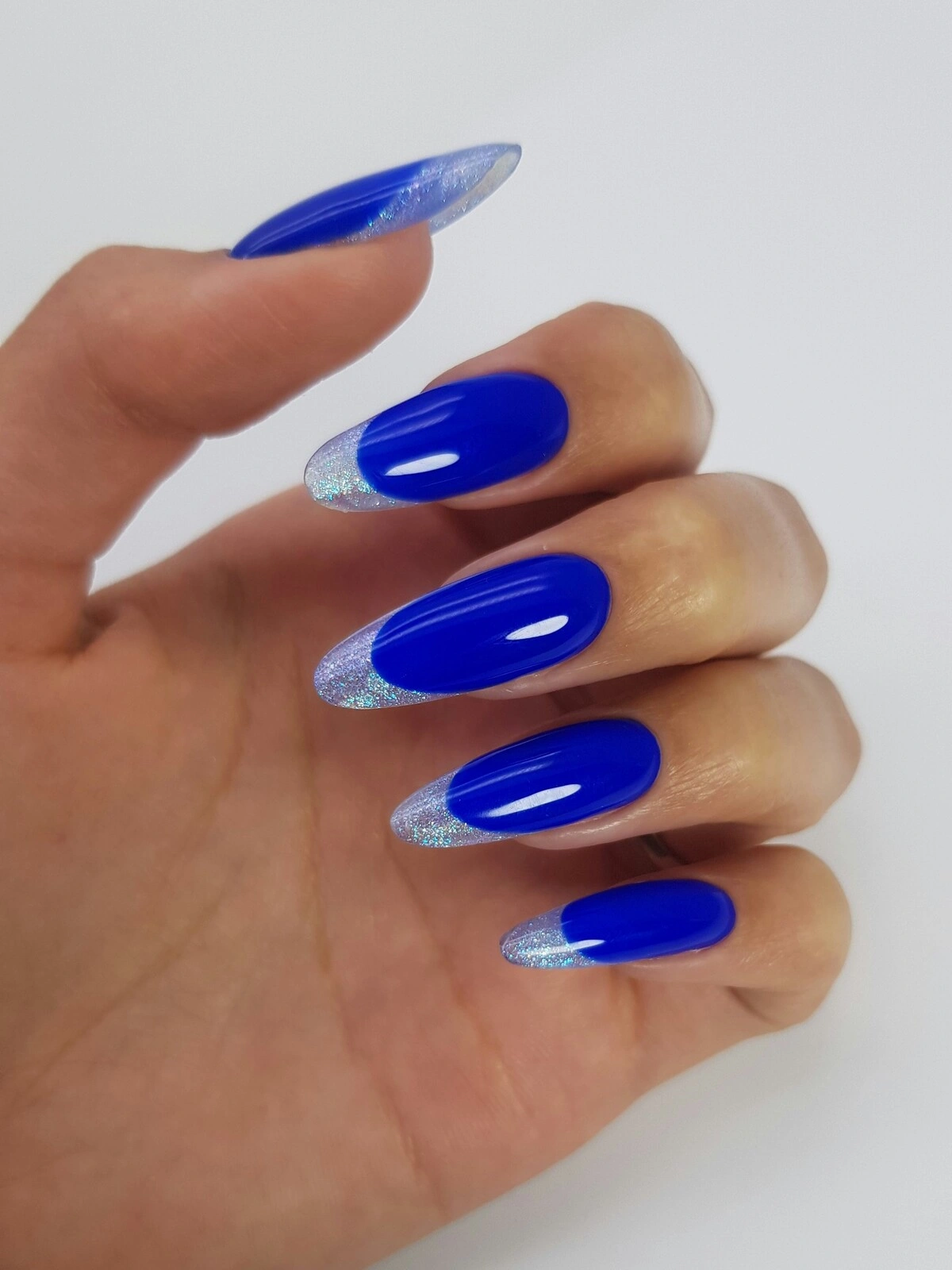 La mano de una mujer con una llamativa manicura francesa de base azul intenso y puntas metalizadas en plata sobre uñas largas de almendra