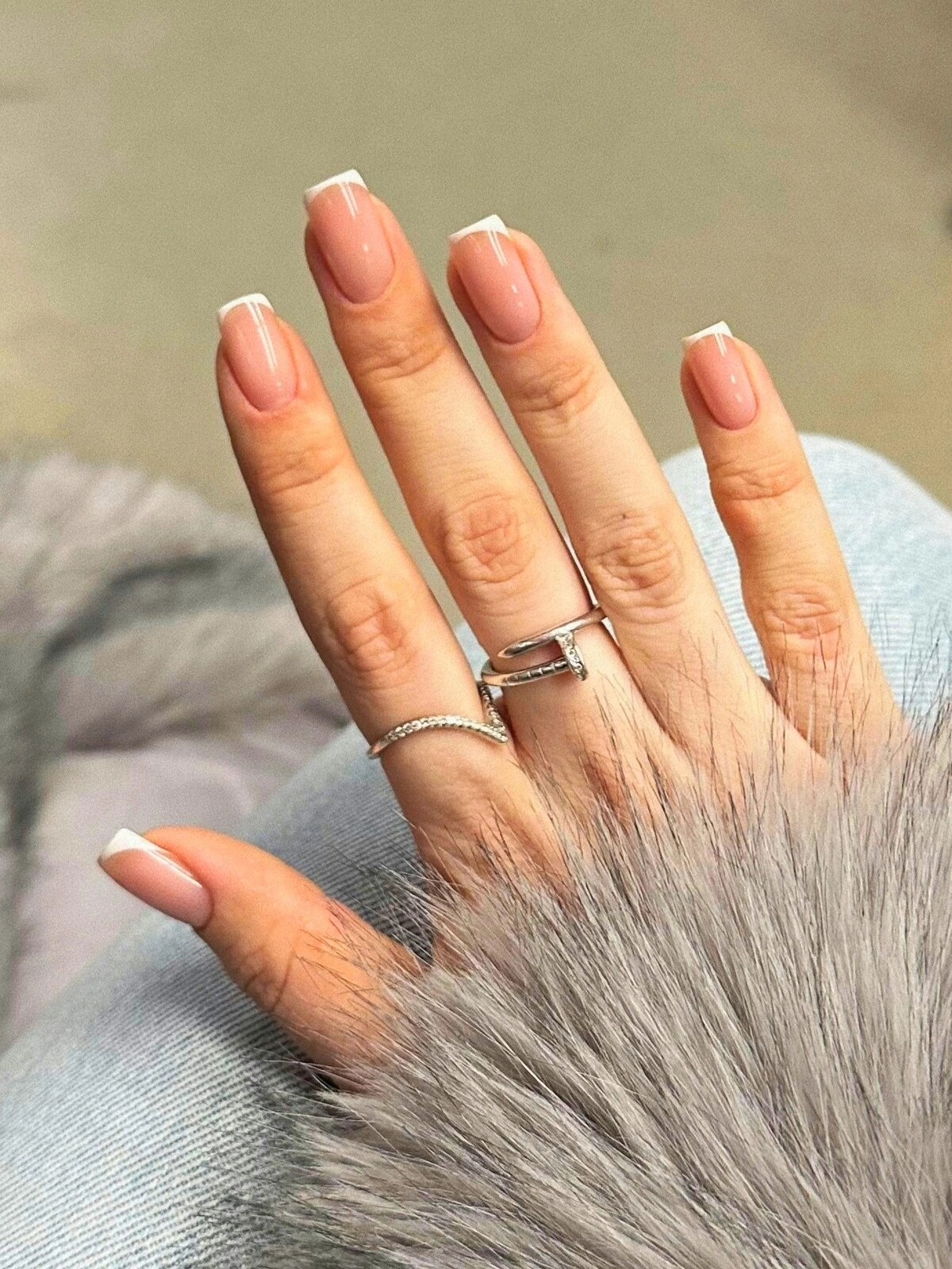 La mano de una mujer con una manicura francesa de micro líneas sobre uñas cuadradas