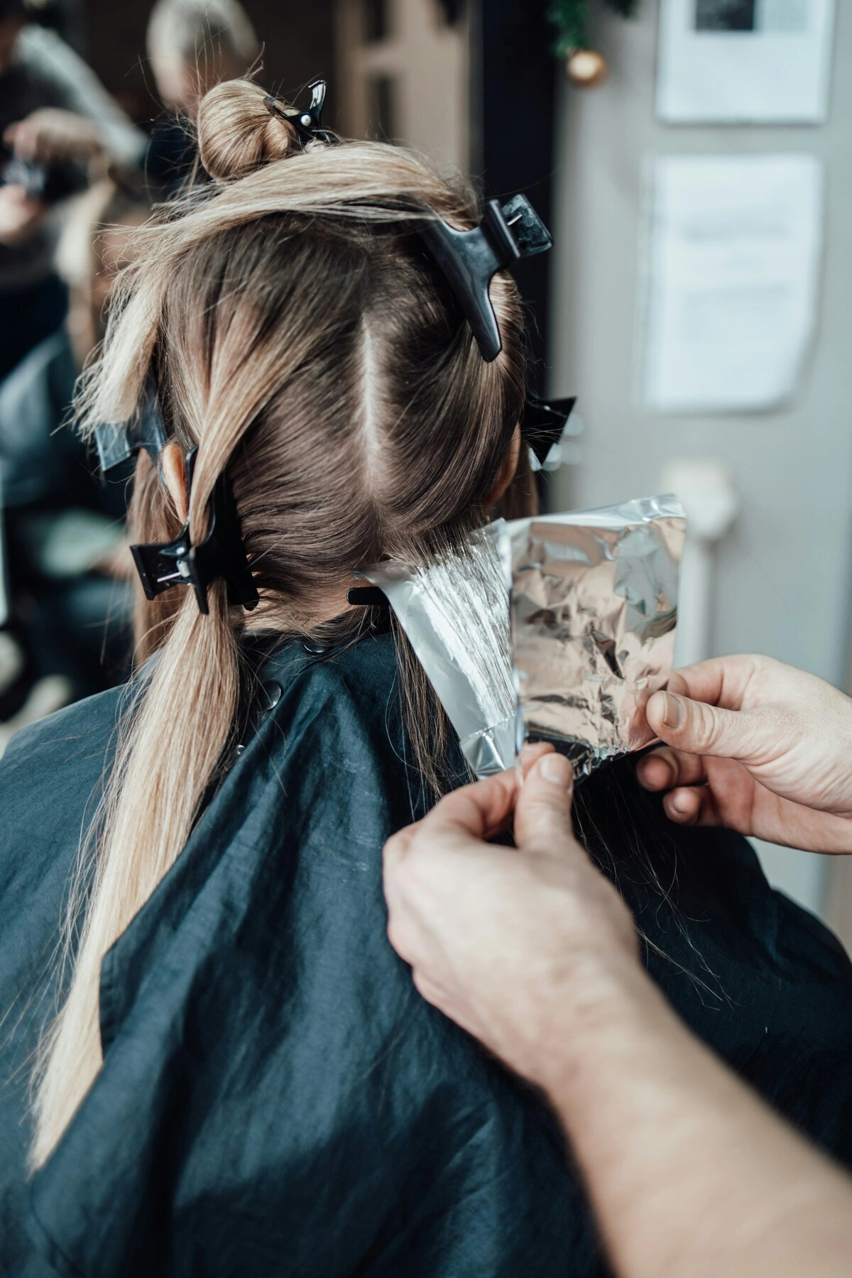 Una clienta vista de espaldas en el sillón de la peluquería mientras la estilista le coloca papel de aluminio en el pelo para las mechas