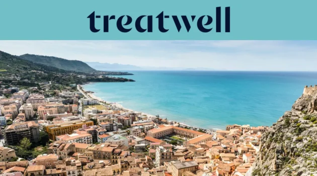 Vista panorámica de un pueblo costero siciliano, con antiguos edificios de tejados de terracota, una media luna de playa de arena, un mar turquesa cristalino y un promontorio rocoso que se alza a un lado.