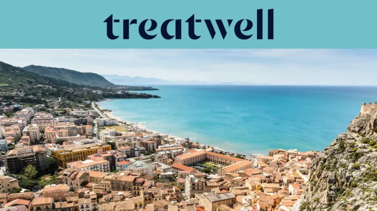 Vista panorámica de un pueblo costero siciliano, con antiguos edificios de tejados de terracota, una media luna de playa de arena, un mar turquesa cristalino y un promontorio rocoso que se alza a un lado.