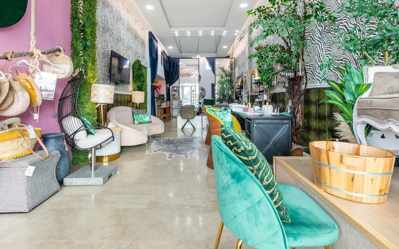 El interior de Brazilian Beauty Marbella, un salón luminoso con paredes de estampado de cebra, una pared vegetal, sillas de terciopelo turquesa y un lavapiés de pedicura de madera.