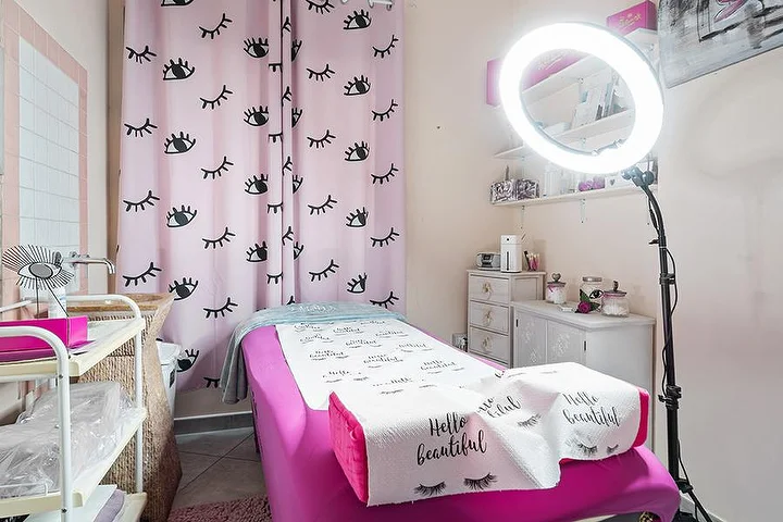 Cabina rosa en Centro Estetico Karma en Olbia con cortinas con estampado de pestañas, camilla de belleza y aro de luz.