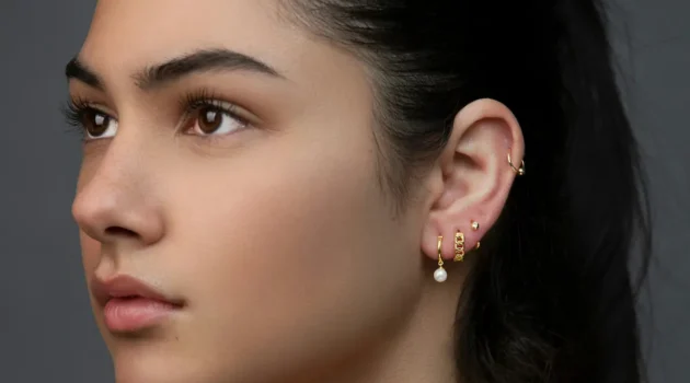 Foto de estudio de una mujer con varios piercings en el lóbulo y un aro en el hélix formando un ear look