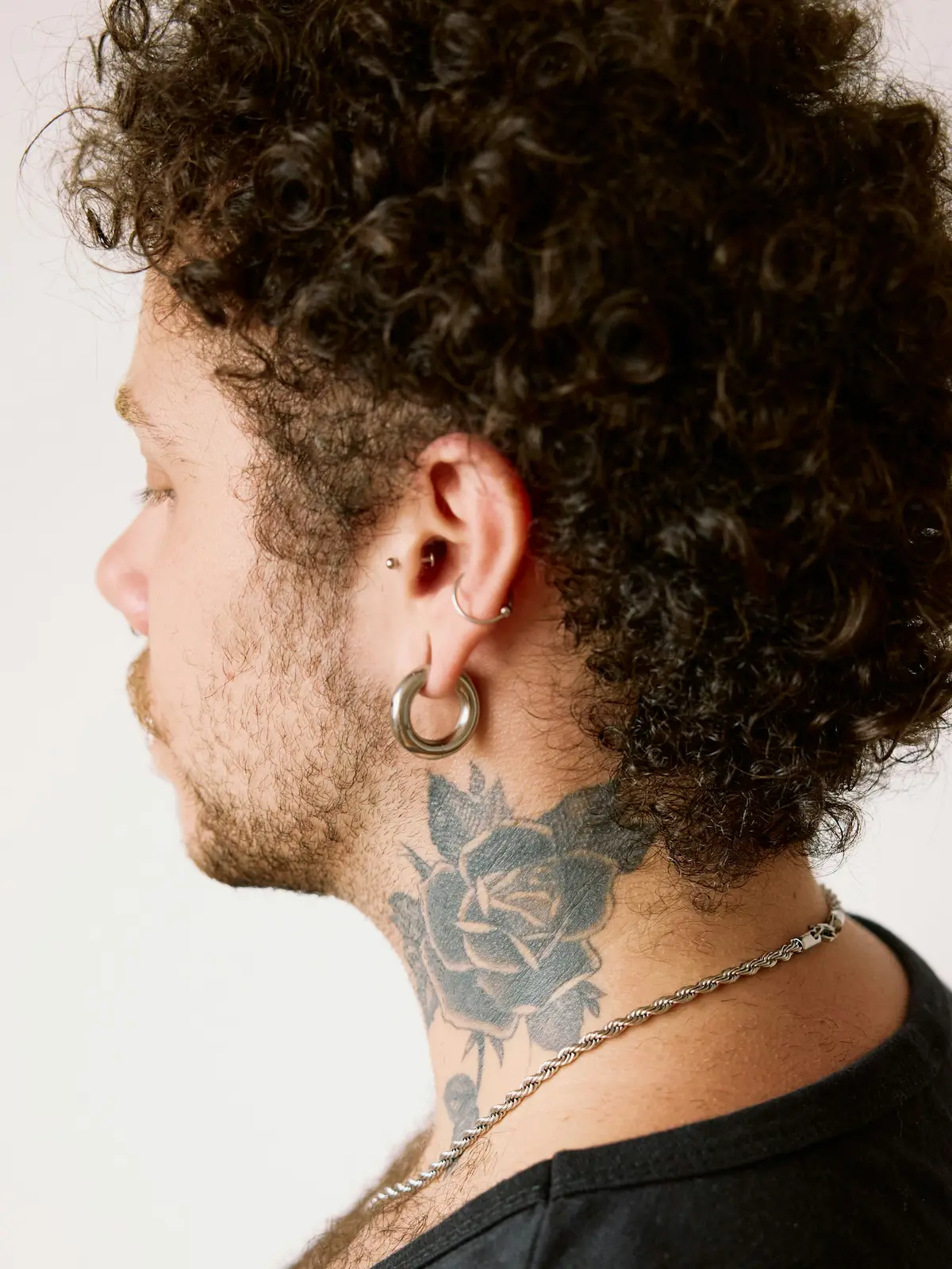 Foto desde atrás de un hombre con piercings en el lóbulo, el hélix y el tragus