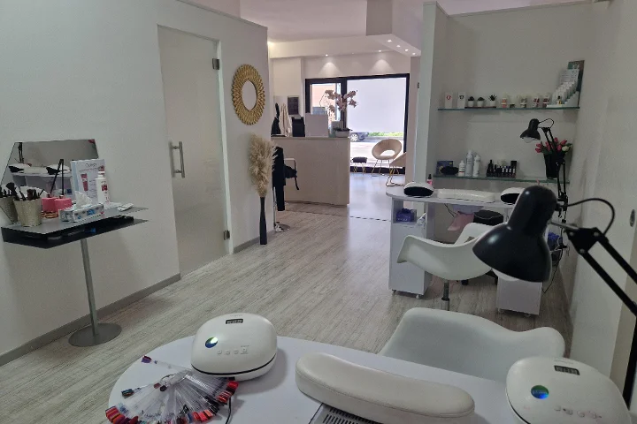 Recepción y zona de manicura en Estetica Francesca en Olbia con espejo redondo en la pared y estanterías de cristal con productos de belleza.