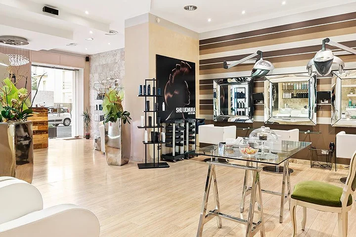 Puestos de peinado elegantes en el salón Hair Queen de Cagliari con paredes a rayas crema y marrones y grandes maceteros plateados.