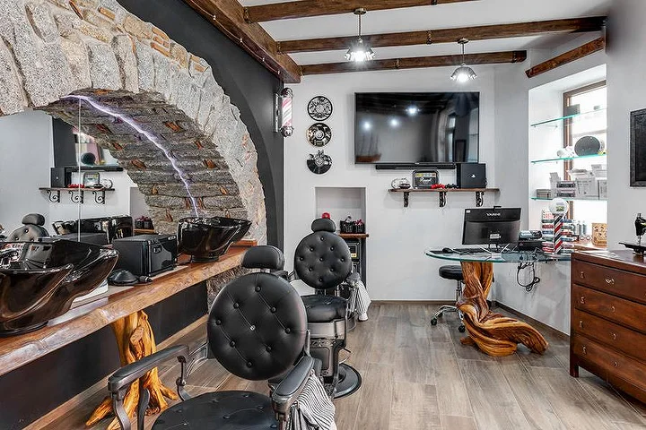Sillón de barbero rústico frente a un arco de piedra en La Bottega di Pablo, en el pueblo de montaña de Lanusei.