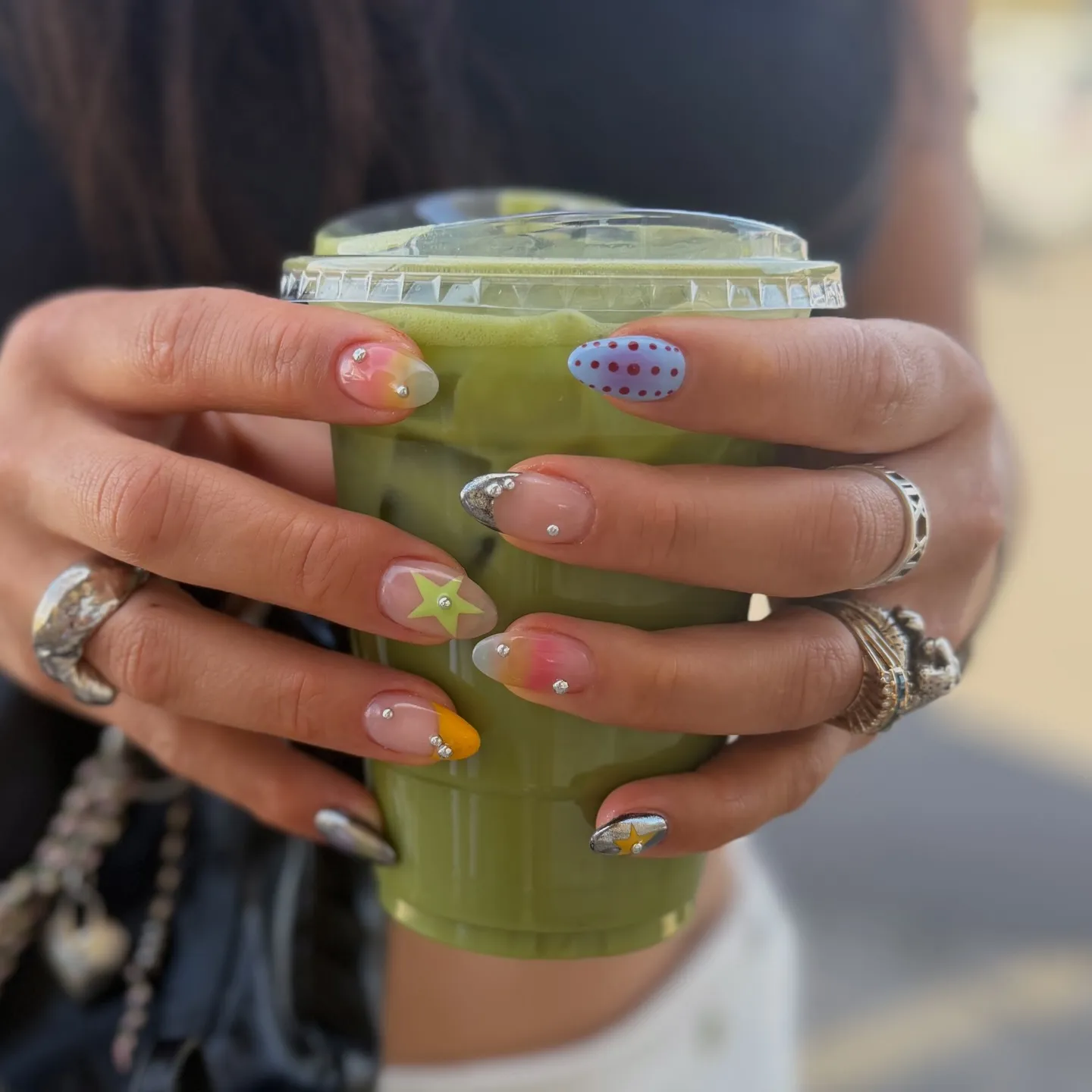 Conjunto variado de nail art con pequeños piercings de cristal, motivos de estrella y toques de color en uñas de forma almendra