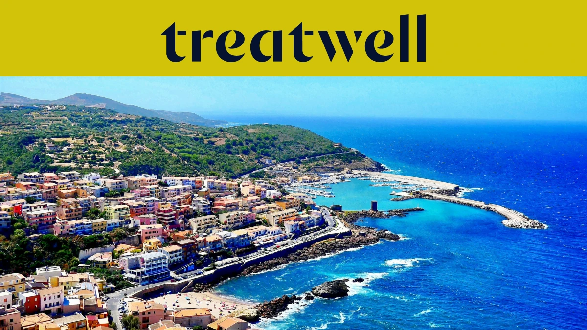 Vista aérea de un pueblo costero sardo con casas de colores pastel, puerto pequeño y mar turquesa.
