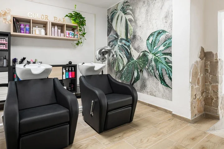 Lavacabezas y color bar en el salón Yourself en Tortolì con un mural de hojas de monstera tropical.