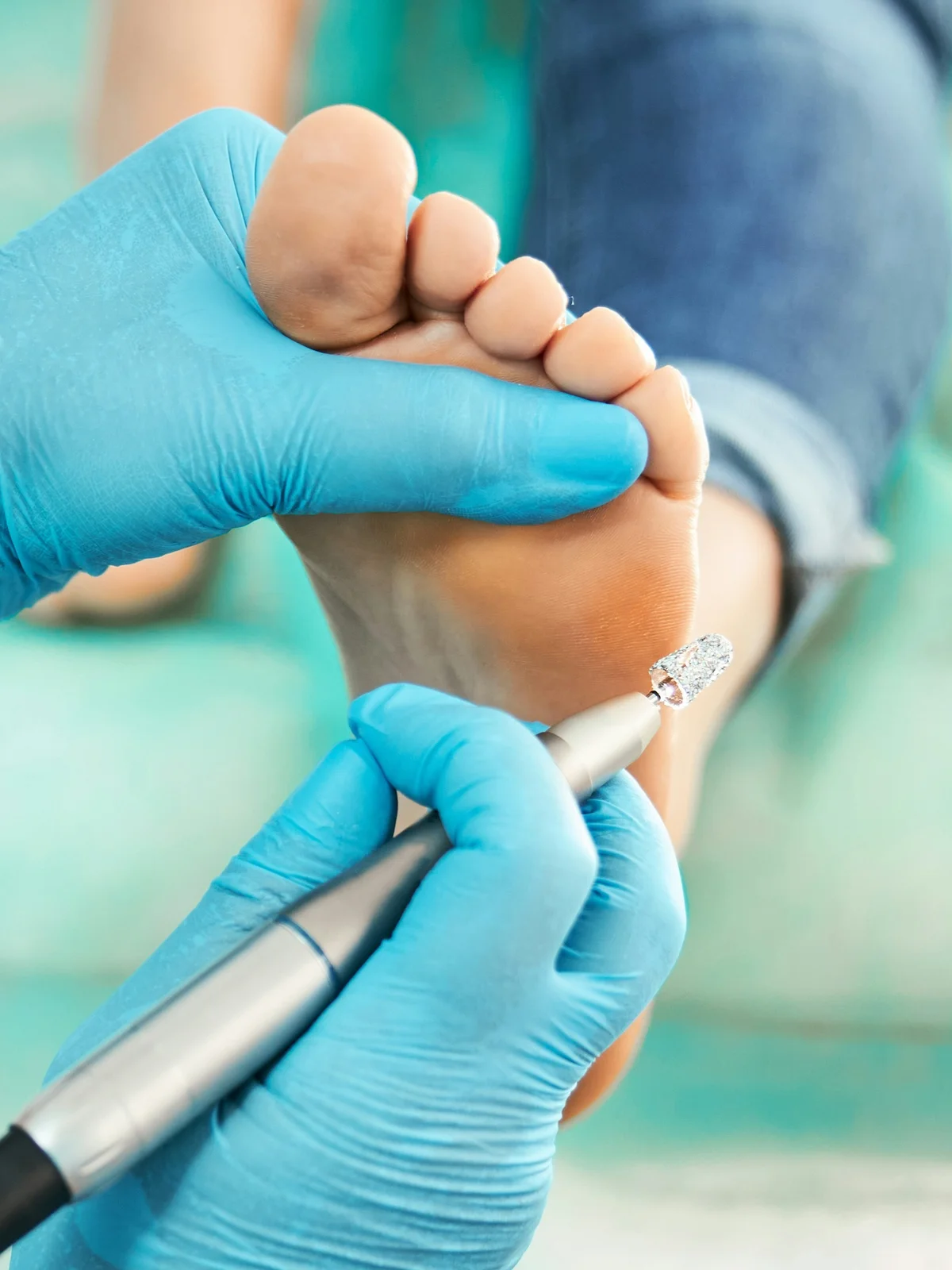 Primer plano de una esteticista con guante que exfolia suavemente el pie de una clienta con un pequeño torno eléctrico
