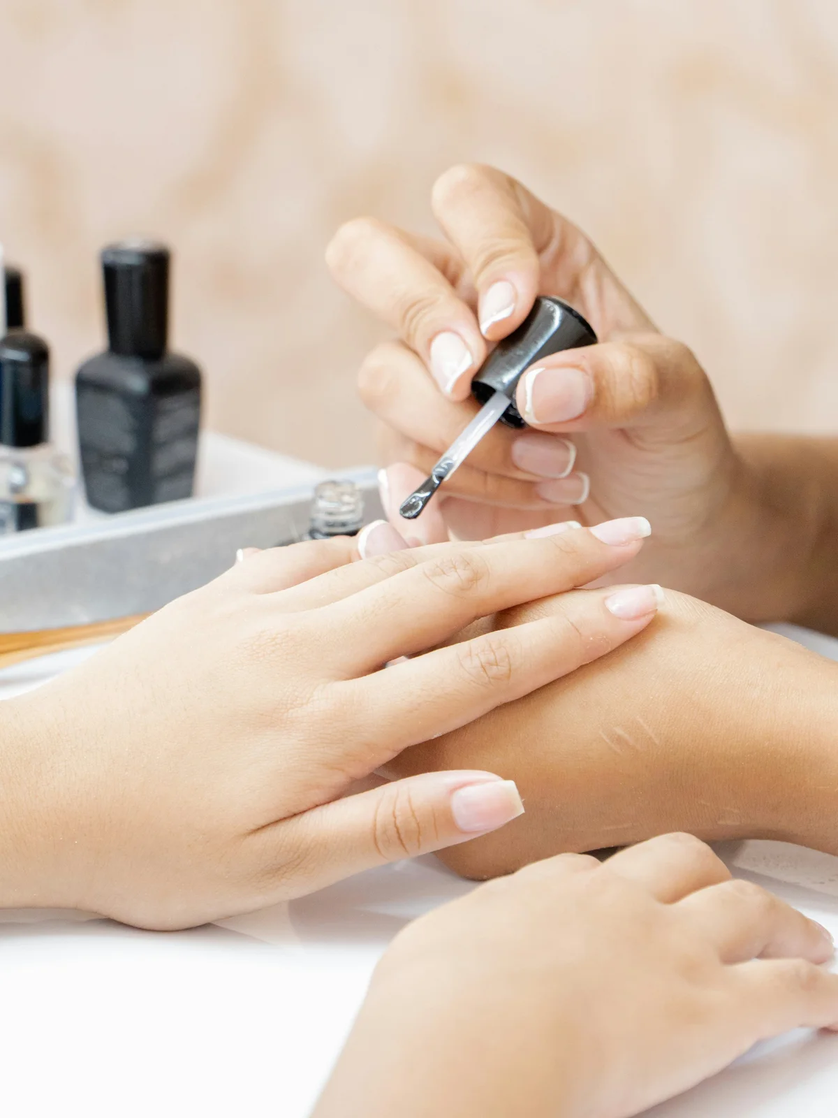 Primer plano de una manicurista aplicando un tratamiento reforzante transparente sobre las uñas de una clienta en el centro