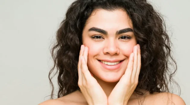 Una joven con la piel limpia y el pelo oscuro y ondulado sonríe a la cámara