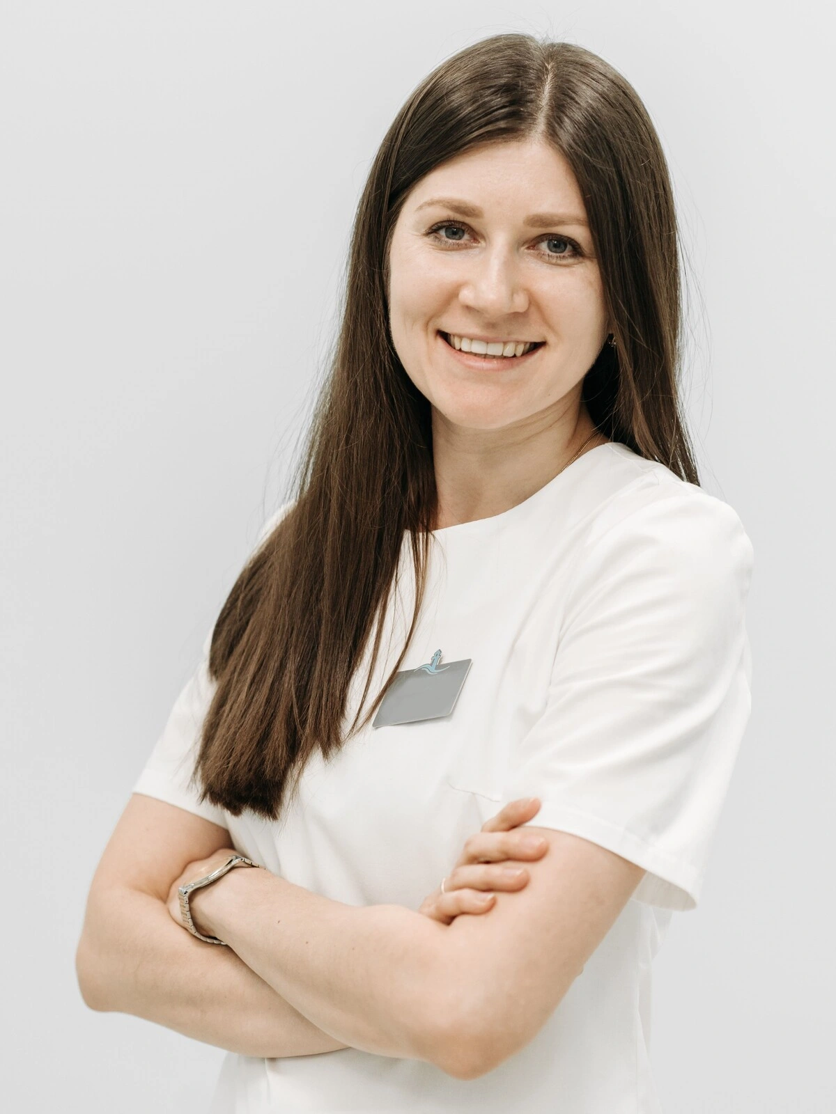 Retrato de una esteticista con túnica blanca sonriendo con los brazos cruzados
