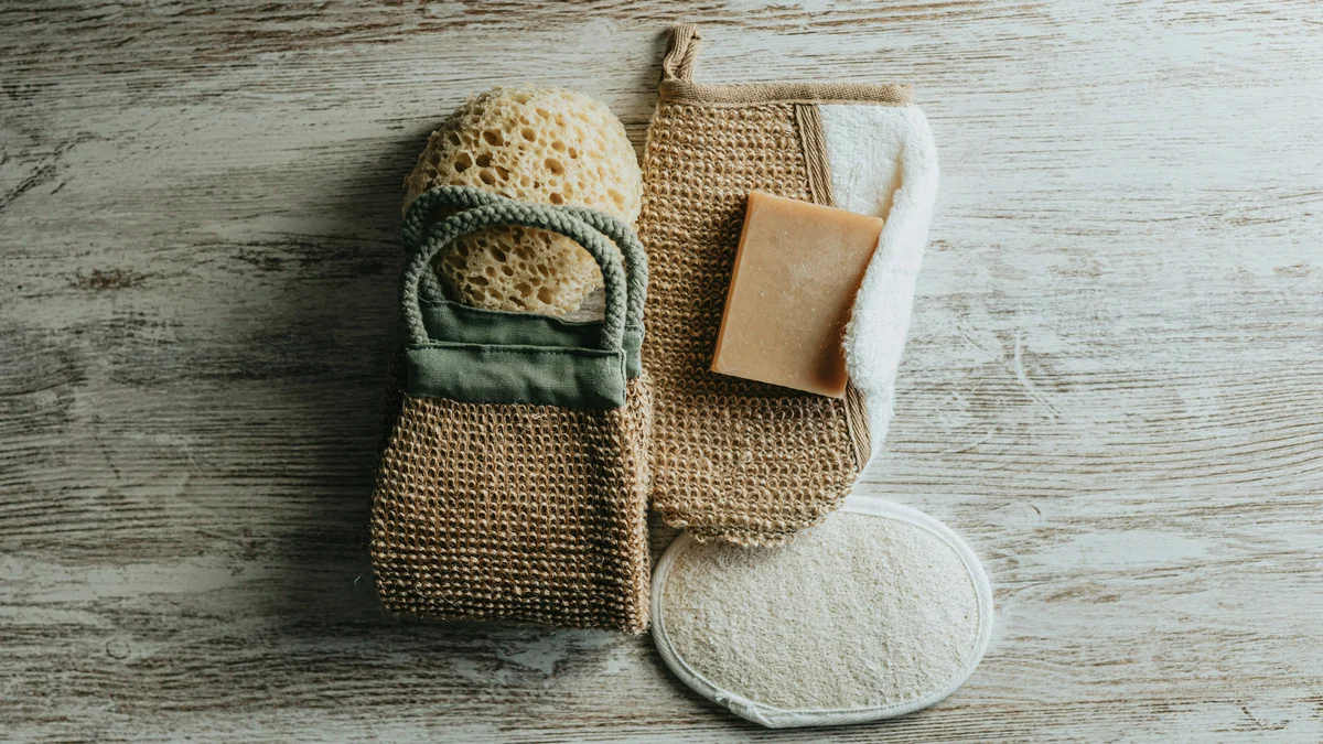 Vista cenital de unos guantes exfoliantes, una esponja natural y un jabón exfoliante