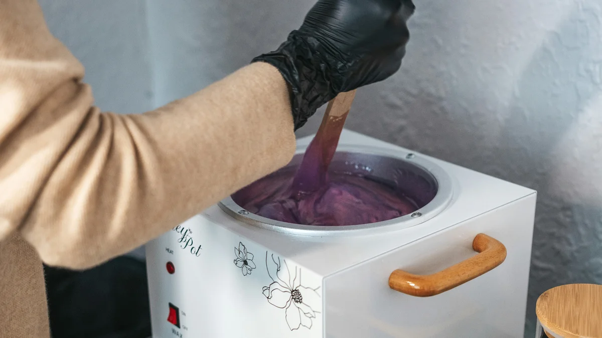 La mano de una esteticista con un guante negro remueve un bote de cera caliente fundida en un centro de estética