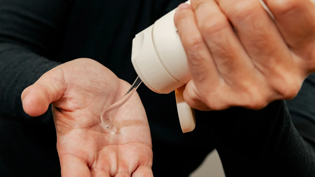 Primer plano de las manos de un hombre que con una mano exprime un tubo blanco de gel hidratante sobre la otra mano