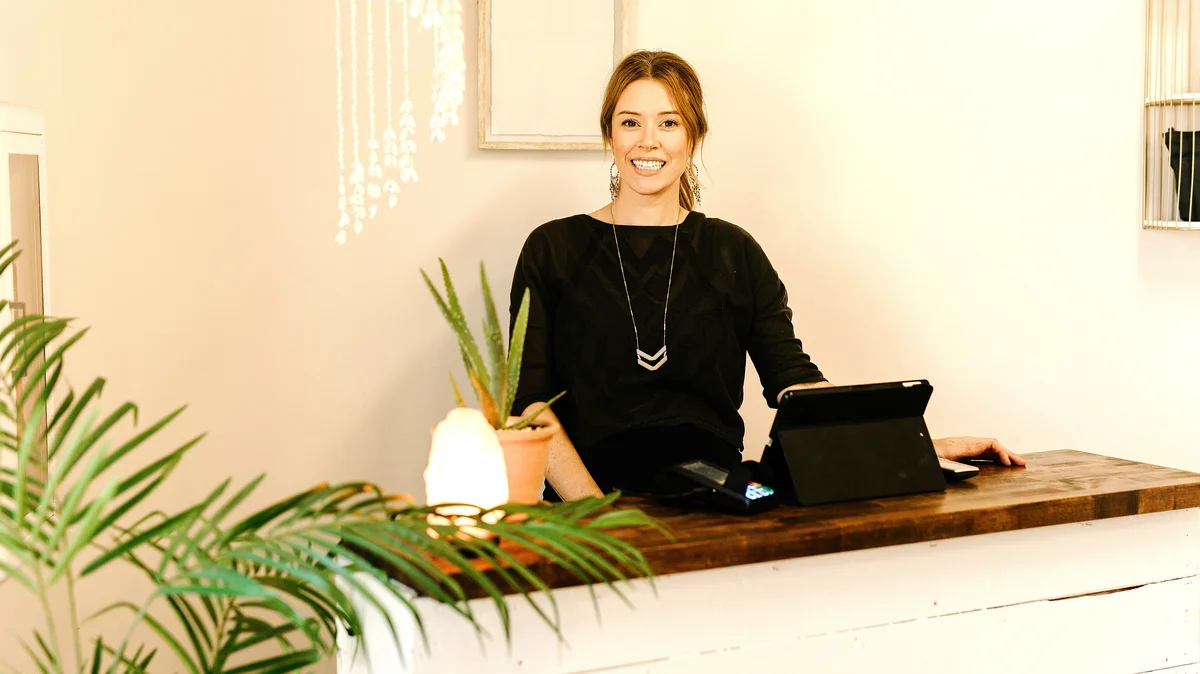 Una mujer sonriente está detrás del mostrador de recepción de un centro de estética