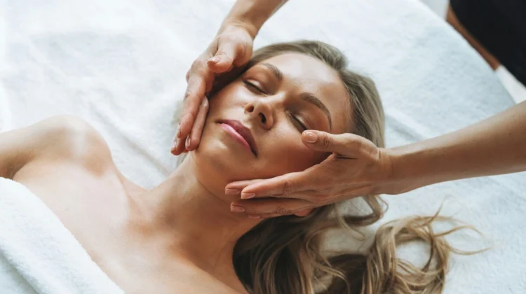Mujer relajada durante un masaje facial de drenaje linfático suave, con las manos de la profesional deslizándose ligeras por su rostro